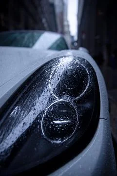 Closeup of the sharp angular headlight of a white Porsche covered in raindrops o Fotos de archivo