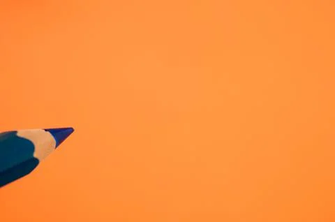 Closeup of a sharp blue pencil isolated on an orange background Stock Photos