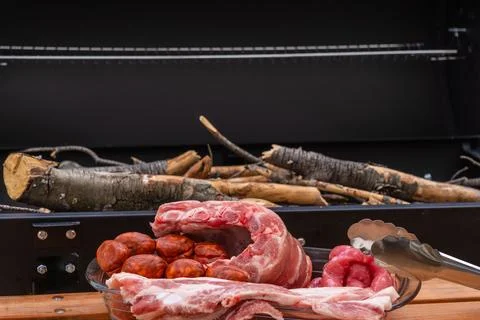 Closeup shot of an array of raw meats near an outdoor grill with wood Stock Photos