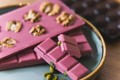 Closeup shot of bars of sweet ruby chocolate with walnuts and pistachios Stock Photos