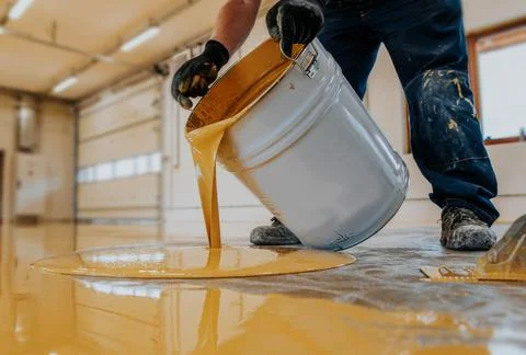 A closeup shot of a construction worker pouring out epoxy resin from a bucket Stock-Fotos