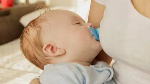 Closeup shot of cute baby boy with soother fell asleep on mothers hands Stock Footage