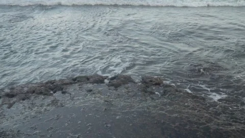 Closeup shot of foams created by the ocean waves meet a rocky shoreline. Stock Footage 312860451