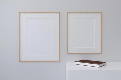 Closeup shot of frames on a white wall with a book on a shelf Stock Photos