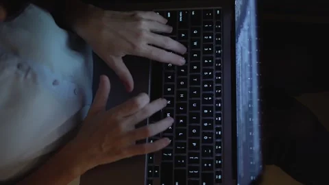 A CloseUp Shot of Hands Typing Rapidly on a Laptop Keyboard in a Dimly Lit Room Stock Footage 289965288