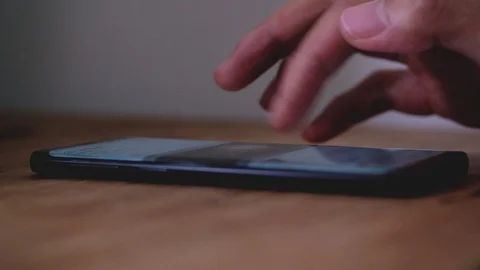 Closeup shot of man scrolling screen on smartphone on a wooden table. Stock Footage 100403564