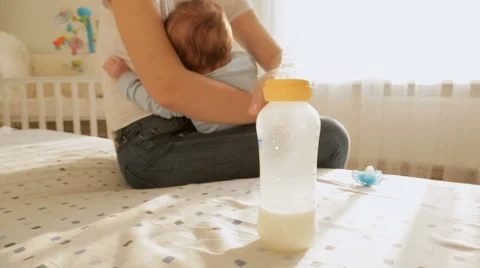 Closeup shot of mother with her baby sitting on bed, taking bottle of milk an Stock Footage