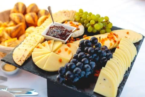 Closeup shot of processed cheese with jam and grapes on a black tray Foto stock