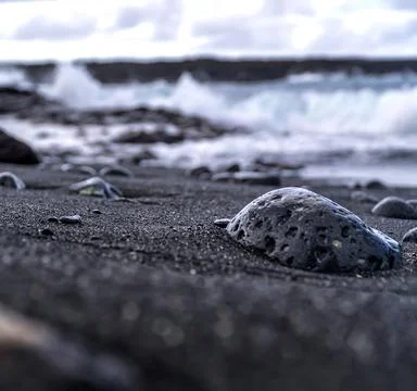 Closeup shot of a rock on the beach with tiny holes with waves in the background 写真素材