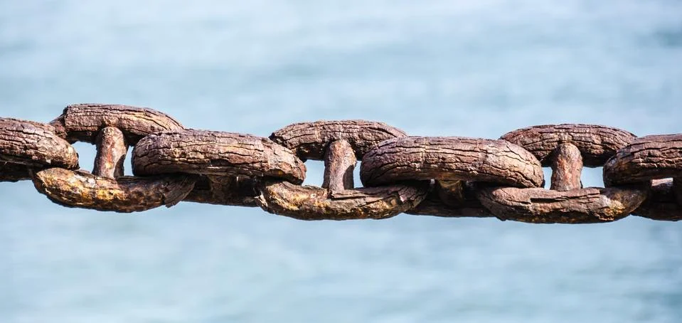 Closeup shot of a rusty old interlinked chain on a blue background Stock Photos