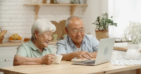 Closeup shot of senior asian couple using a computer, sitting in kitchen and Stock Footage