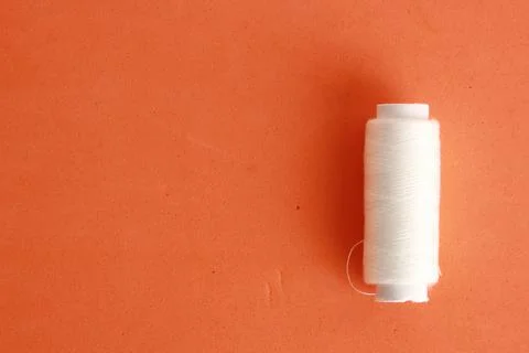 Closeup shot of a sewing thread for white clothes on an orange background 写真素材