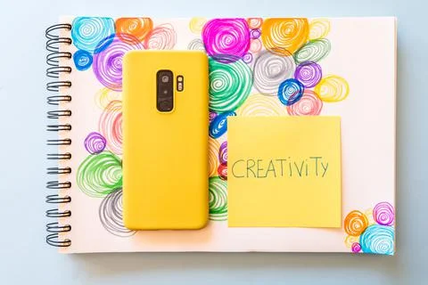 Closeup shot of a sticky note with "Creativity" writing and a cellphone Stock Photos