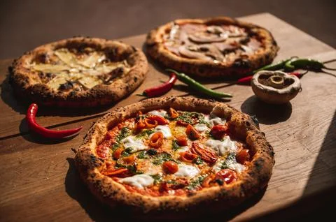 Closeup shot of three types of pizza with chili peppers and mushroom on wooden b Stock Photos