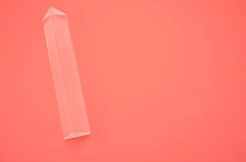 Closeup shot of a triangular glass prism isolated on a red background Stock Photos