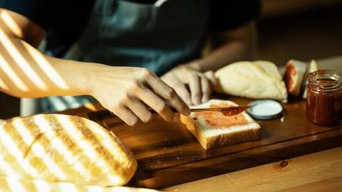 Closeup shot of unrecognizable spreading raspberry jam on slice of bread with Stock Photos