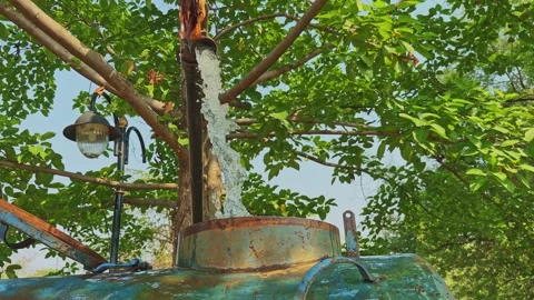 Closeup shot of water pouring into a rusty tanker from a pipe under green trees 스톡 동영상 336680913