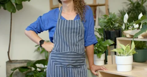 Closeup showing apron, non-binary worker adjusting strap, leaning on shelf Stock Footage 344536175