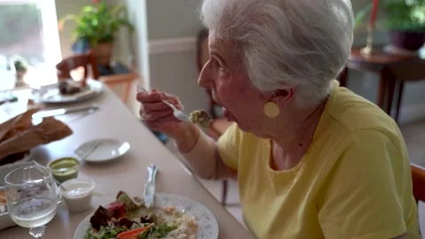 Closeup side view of elderly woman in dining room eating with a glass of wine in Vídeos de archivo 136425919