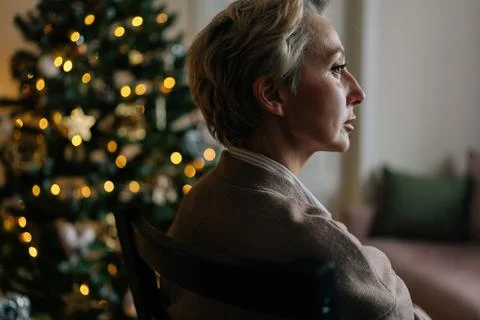 Closeup side view of elegant middle-aged woman sitting in dark living room on Stock Photos