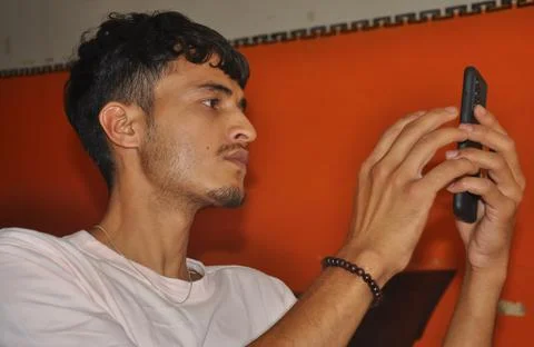 Closeup side view of a young guy using his phone while sitting indoors 写真素材