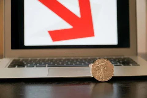 Closeup of silver coins with a drop in value on the computer with red arrow Stock Photos