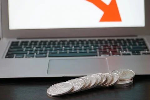 Closeup of silver coins with a drop in value on the computer with red arrow Stock Photos
