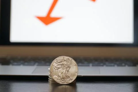 Closeup of silver coins with a drop in value on the computer with red arrow Stock Photos