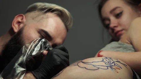 Closeup skilled master makes outline on girl thigh tattoo Stockbeeldmateriaal 104863773