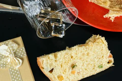 Closeup of a slice of Panettone next to a gift box and an overturned glass of Stock Photos