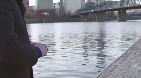 Closeup slow-mo view of man skipping rocks from a dock by a bridge in city Stock Footage 60072007