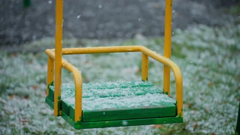 Closeup slow motion of snowflakes falling on empty swings at public playground Stock Footage 258432661