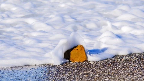 Closeup of small rock on beach as wave and foam crash into and recede-HD120fp Vídeos de archivo 107641521
