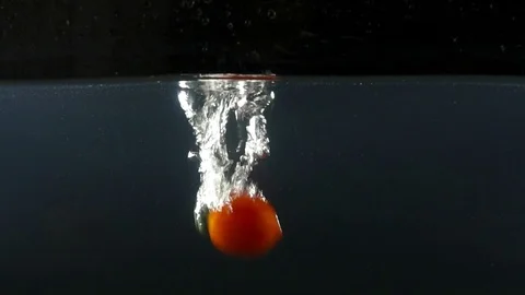 Closeup of small tomatoes falling into water on the black backgrond slow motion Stock Footage 75790473