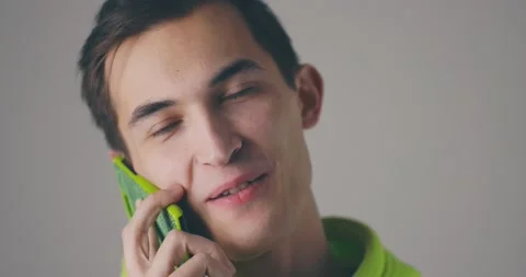Closeup smiling young handsome man speaking phone emotionally at grey wall 스톡 동영상 148052789