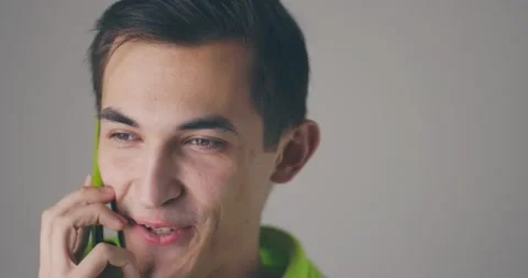 Closeup smiling young handsome man speaking phone emotionally at grey wall Stock Footage 148396156