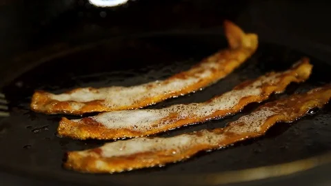 Closeup of some tasty strips of bacon frying in a pan with a man turning over Stock Footage 124397276