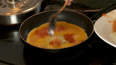 Closeup of spatula adding tomato to an omelet cooking on stove top Vídeos de archivo 128451158