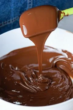 Closeup of a spatula with tempered chocolate falling into a white bowl. Stock Photos