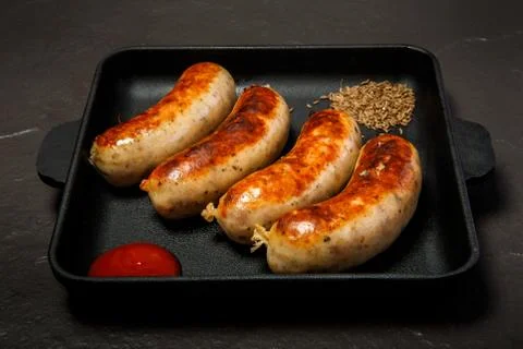Closeup square pan with four fried sausages, ketchup, caraway seeds 写真素材