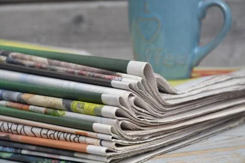 A closeup of the stack of newspapers with a cup of coffee isolated on a woode 스톡 사진