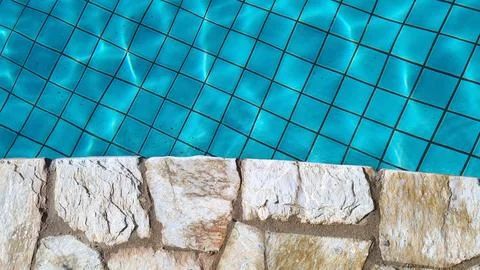 Closeup of stone border in front of bright blue swimming pool. Stock Photos