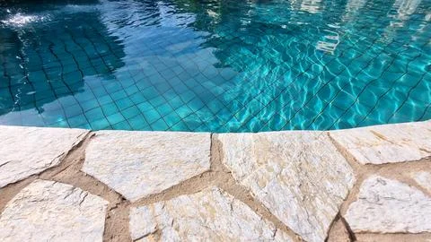 Closeup of stone border in front of bright blue swimming pool. Stock Photos