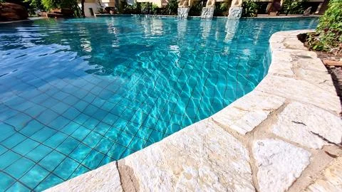 Closeup of stone border in front of bright blue swimming pool. Stock Photos