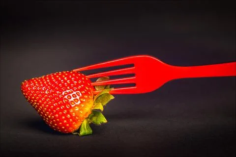 Closeup of a strawberry on a red fork Stock Photos