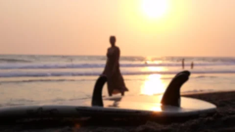 Closeup of surfboard at sunset on beach. Behind surfboard notice people passing Stock Footage 257335870