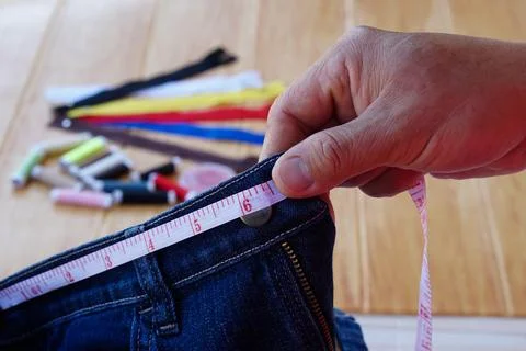 Closeup tailor hand use measuring tape to measure width of jeans waist. Stock Photos