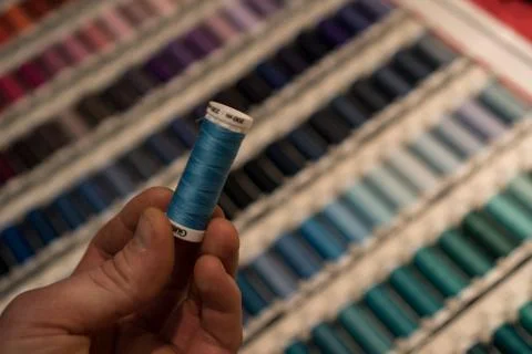 Closeup of tailors hands choosing thread color from box of different sewing Stock Photos