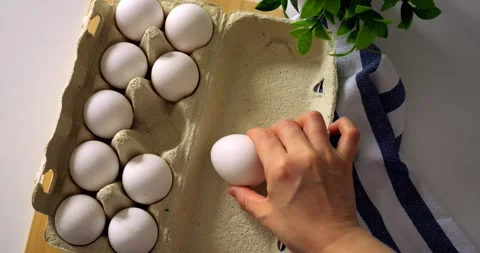 Closeup of taking fresh egg from open carton on wooden table with striped towel Stock Footage 315692661