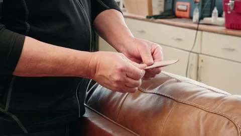 Closeup of Technician Preparing Sandpaper to Refinish Brown Leather Sofa Stock Footage 309105710